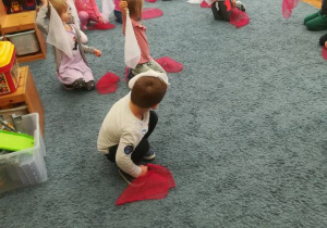 Dzieci podczas zabawy z chustkami biało – czerwonymi utrwalają barwy narodowe – wysoko – unoszą białą chustkę, czerwona chustka nisko na dywanie.
